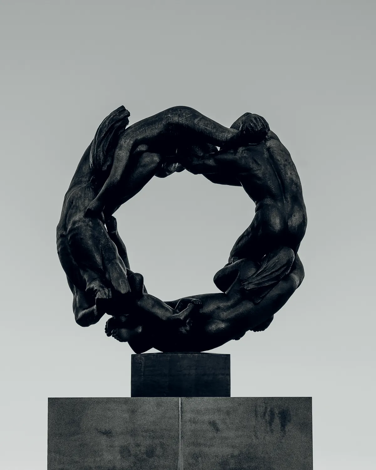 A dark bronze ring of figures on a plinth against a pale sky, the centre of it empty