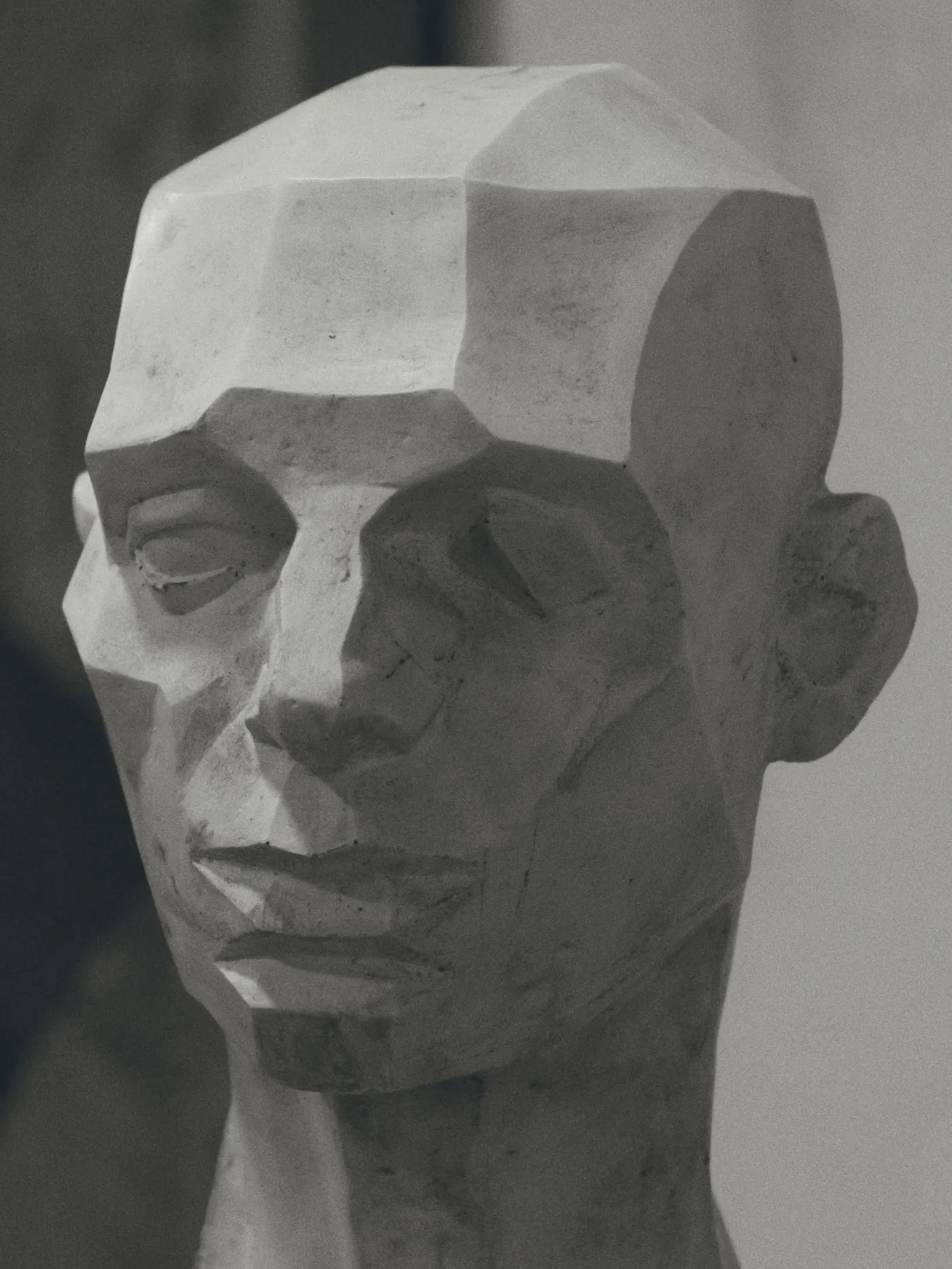 A plaster study head cut down to its flat planes, lit hard from the left
